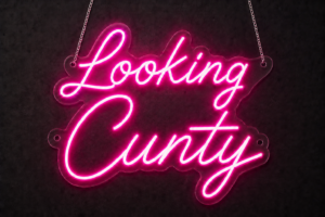 Looking Cunty neon sign in hot pink LED neon script on clear acrylic, hanging on chains against a dark wall
